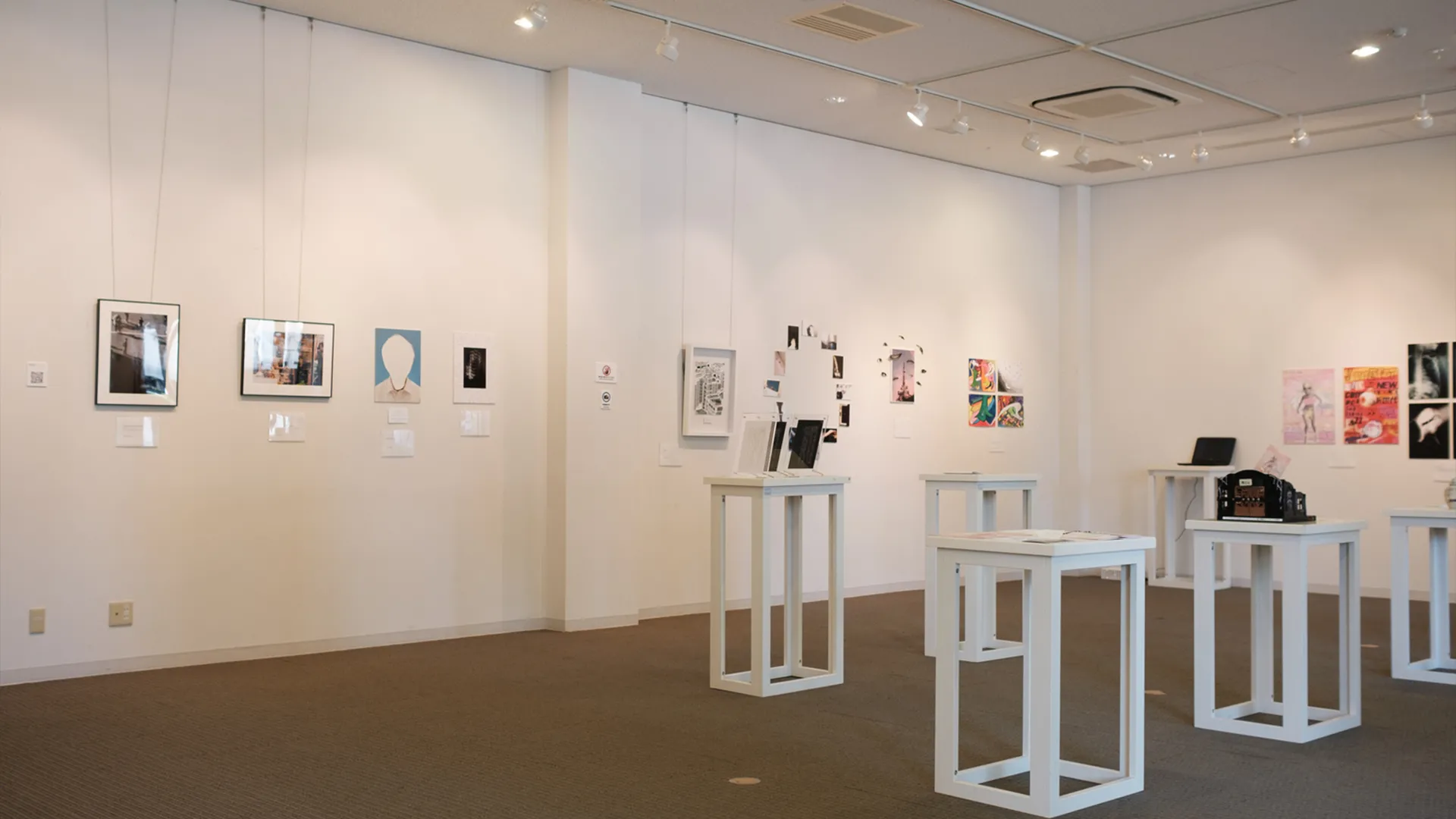 "自己中心展 -Mirror, Mirrors-"の会場風景。白い壁のギャラリーに6台の展示台が置かれ、壁と展示台の両方に作品が展示されています。