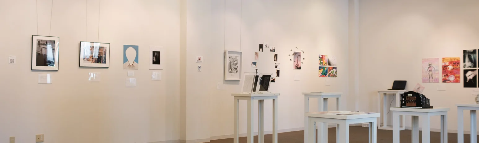 '自己中心展 -Mirror, Mirrors-'の会場風景。白い壁のギャラリーに6台の展示台が置かれ、壁と展示台の両方に作品が展示されています。